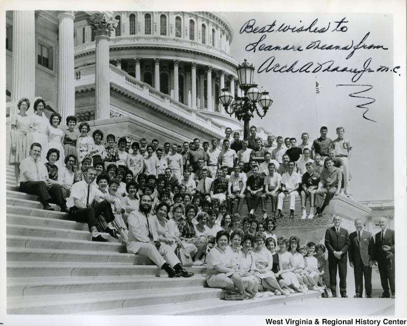 Congressman Arch Moore, Jr. and a group of unidentified people sitting on the steps of the Capitol building. The photograph is signed, "Best wishes to Leanore Means from Arch A. Moore, Jr.  m.c."