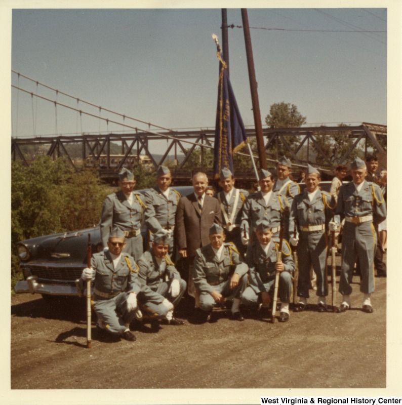 Congressman Arch A. Moore, Jr. (center) with an unidentified honor guard. They are standing in front of a vehicle, and the Market Street Bridge can be seen in the background.