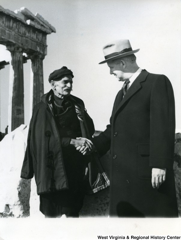 Congressman Arch A. Moore, Jr. shaking hands with an unidentified Greek man in Athens, Greece. The Parthenon can be seen in the background. A note, in Greek, is written on the back of the photograph.