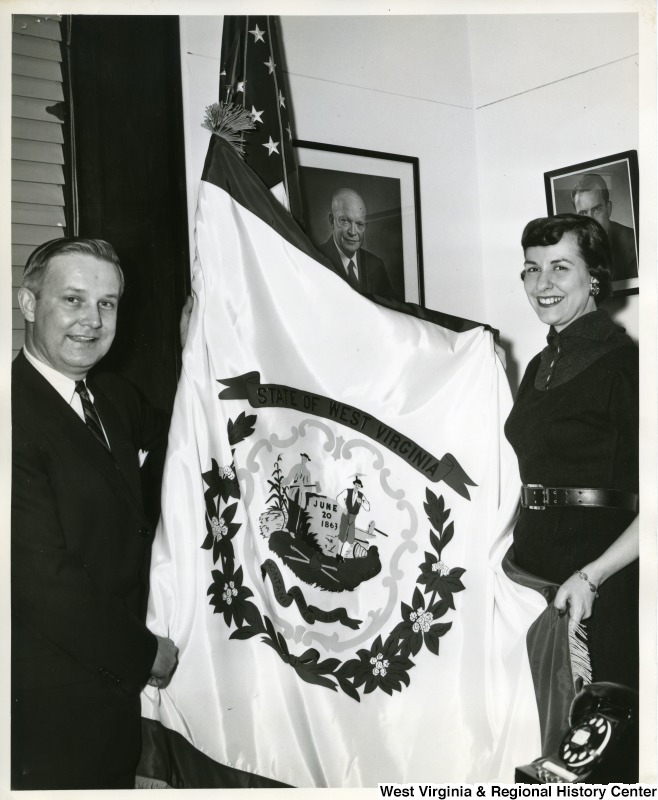 Congressman Arch A. Moore, Jr. and his secretary, Alice Jane Dunn, are unfurling the West Virginia flag in the Congressman's Washington office.
