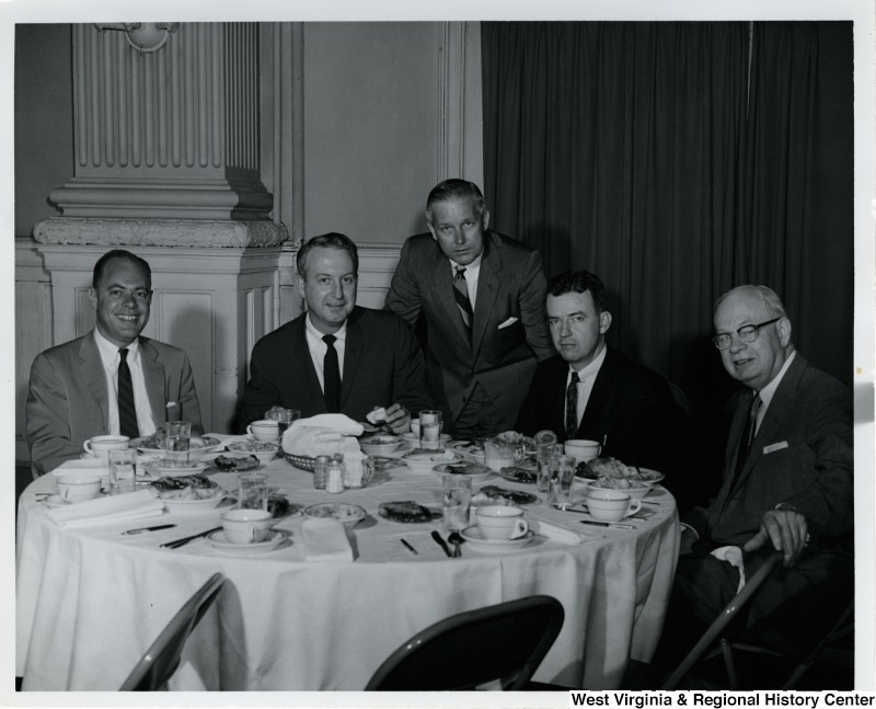 Congressman Arch A. Moore, Jr. standing behind a table where four unidentified men are sitting.