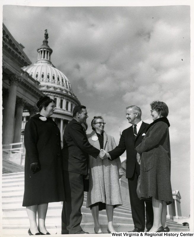 Congressman Arch A. Moore, Jr. shaking hands with an unidentified man. Three unidentified women are standing with them watching.