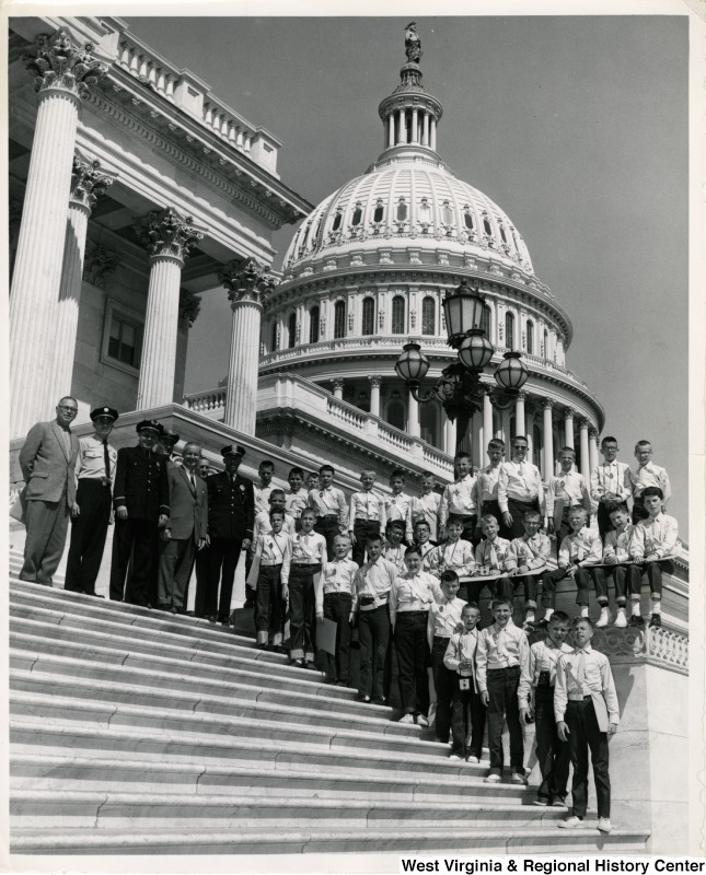 Congressman Arch A. Moore, Jr. standing on the steps of the Capitol with an unidentified group of boys. The boys are wearing uniforms with sashes and badges.