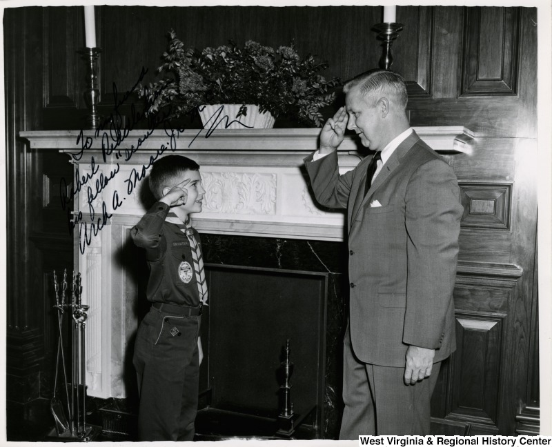 Congressman Arch A. Moore, Jr. saluting Cub Scout Robert (Bobby) Riddle, II in the Sam Rayburn Reception Room. Riddle presented Moore with a Boy Scout emblem to celebrate the 54th anniversary of the Boy Scouts of America to wear during Scout Week (February 7-13). The photograph is signed: " To my friend Robert Riddle from his fellow 'scouters.' Arch A. Moore, Jr. M.C."