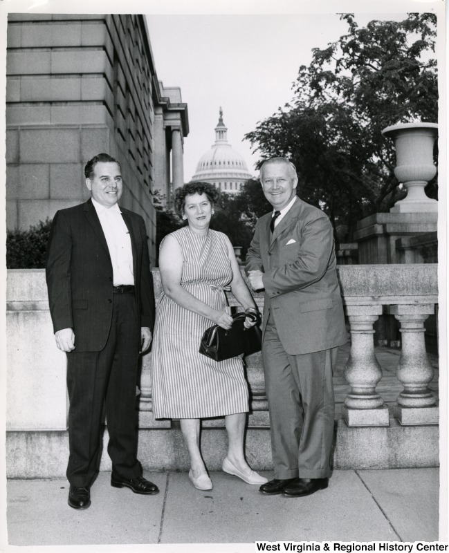 Congressman Arch A. Moore, Jr. standing with a unidentified man and woman. The Capitol Building can be seen in the background.