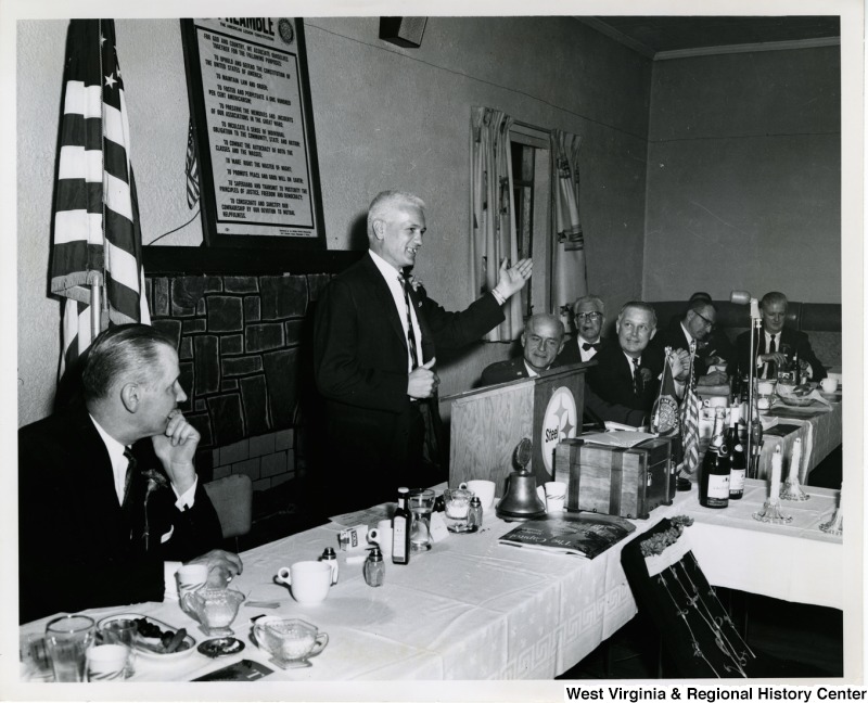 Congressman Arch A. Moore, Jr. seated at a table with other unidentified men listening to an unidentified man from Weirton Steel speak.