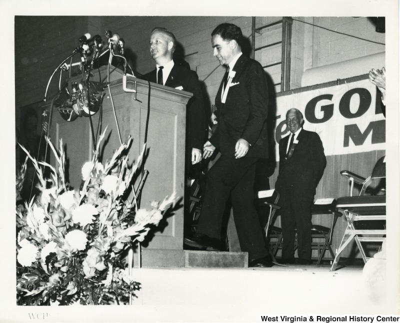 Governor Cecil H. Underwood walking up to a podium while Congressman Arch A. Moore, Jr. is standing beside him at a Goldwater/Miller rally.