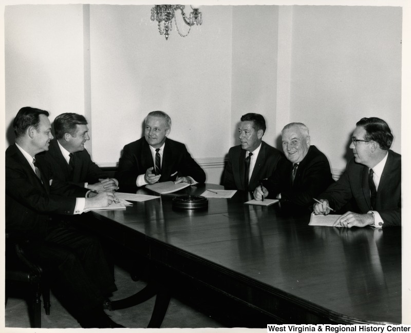 Congressman Arch A. Moore, Jr. sitting with a five unidentified men. They all have documents in front of them and appear to be discussing them.