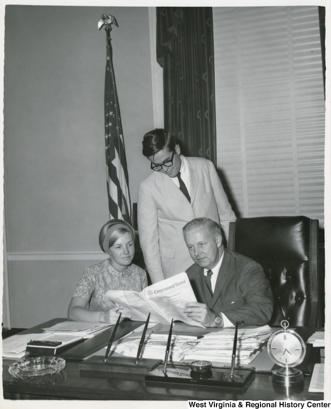 Congressman Arch A. Moore, Jr. seated at his desk showing two of his interns the Congressional Record.