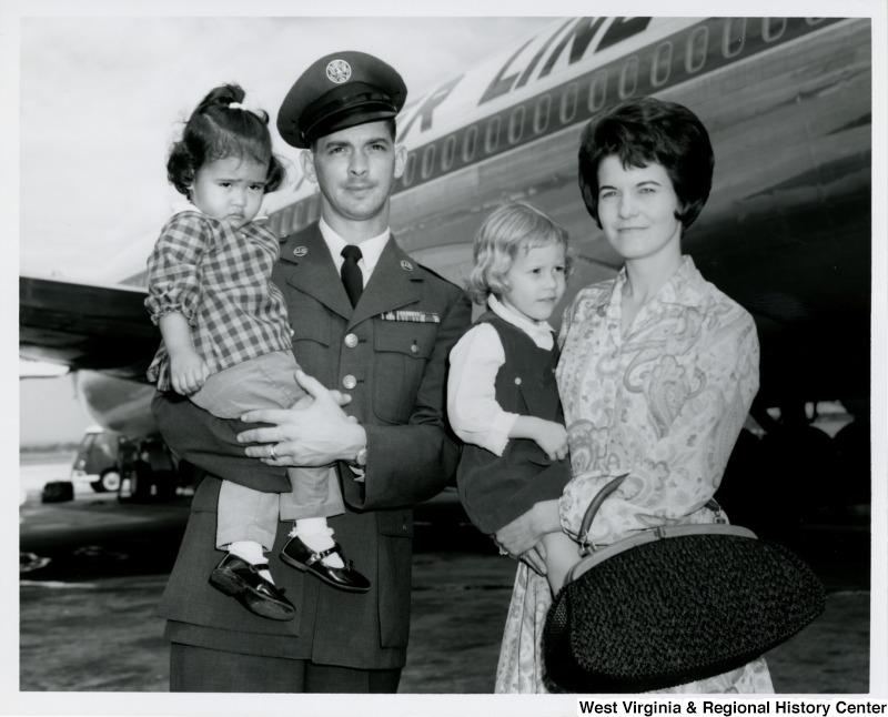 An unidentified couple holding two little girls. A plane is in the background.