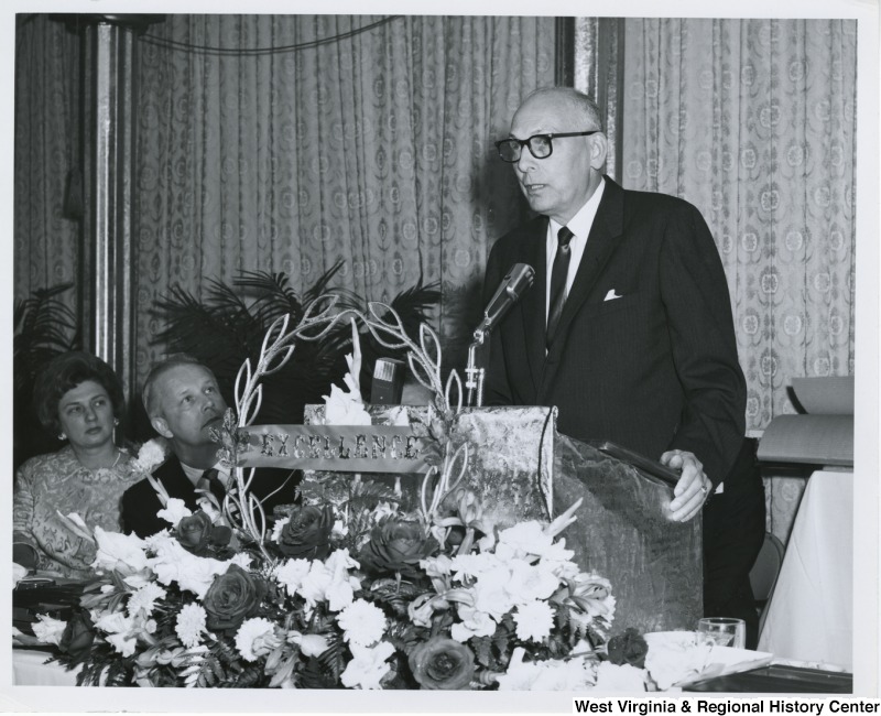 An unidentified man is speaking at the Italian Sons and Daughters banquet in Weirton, W.Va. Congressman Arch A. Moore, Jr. and his wife, Shelley, are seated to the left of the speaker.