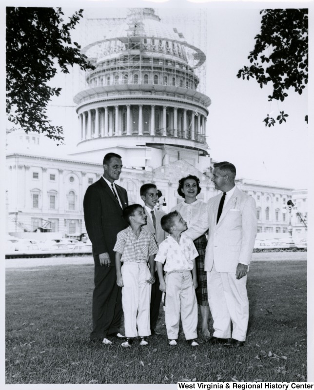 Congressman Arch A. Moore, Jr. standing on the lawn of the Capitol with an unidentified family of five. The Capitol dome is under construction in the background.