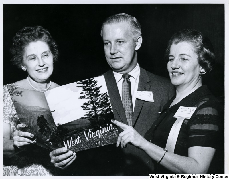 Congressman Arch A. Moore, Jr. with two unidentified women looking at a book of West Virginia. Moore and the woman on the right are wearing Republican National Convention 1960 badges.