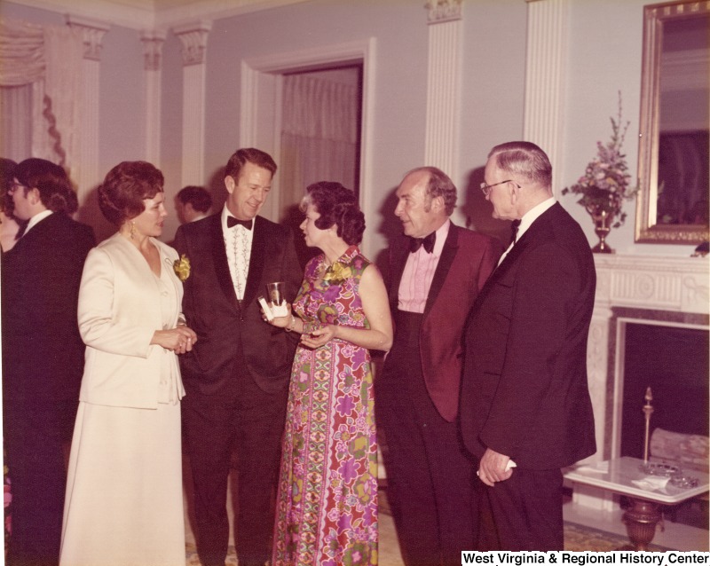 Three unidentified men and two women standing and talking at a reception.