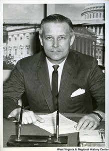 Congressman Arch Moore, Jr. is sitting behind his desk. He is looking at the camera and a letter is laying in front of him.