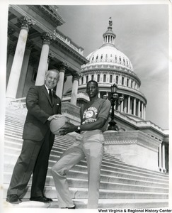 Congressman Arch A. Moore, Jr. holding a basketball with WVU prospect Carl Head on the steps of the Capitol Building. An attached news release states: Operation Head Start - West Virginia University basketball prospect Carl Head (with the WVU monogram) gets some pre-school indoctrination on the steps of the nation's Capitol from Congressman Arch A. Moore, Jr. of West Virginia's First District. Head has been working this summer in his native Washington for the U.S. Post Office. The 6-4 junior college transfer student was the first prospect signed by new WVU basketball coach Bucky Waters. Head was a junior college All-American last year for Dodge City, Kansas. Moore is a WVU alumnus. The congressman's brother, Harry (Moo) Moore of Moundsville, is a former Mountaineer basketball star.