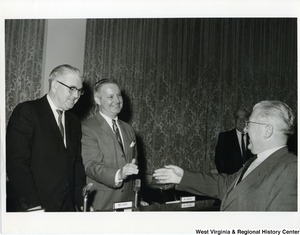 Congressman Arch A. Moore, Jr. shaking the hand of a unidentified man. Congressman Thomas "Tom" Steed is standing beside Moore.