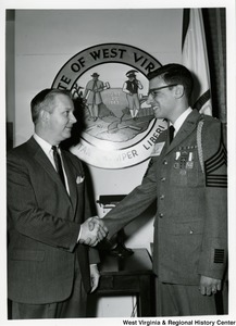 Congressman Arch A. Moore, Jr. shaking hands with an unidentified  man. The man has a pin on his chest stating "I speak for democracy."