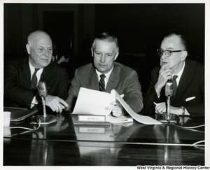 Congressman Arch A. Moore, Jr. discussing a document with two others. A witness plaque is in front of Moore.