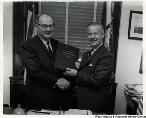 Congressman Arch A. Moore, Jr. and an unidentified man holding the Weirton Steel Employees Bulletin Volume 30, January through December 1963. The two men are also shaking hands.