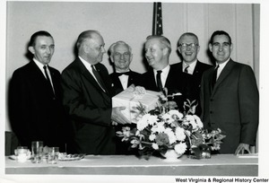 Congressman Arch A. Moore, Jr. receiving a gift from an unidentified man. Four other men are standing around them.