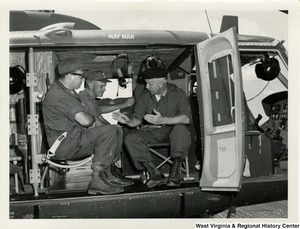 Congressman Arch A. Moore, Jr. sitting in the back of a helicopter talking to two unidentified men in uniform.