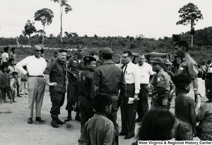 Congressman Arch A. Moore, Jr. talking to an unidentified group of men in the Kon Tum Province of Vietnam. They are surrounded by children and adults.