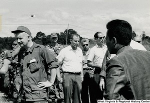 Congressman Arch A. Moore, Jr. standing, in the left corner, and looking at something. He is surrounded by a group of unidentified men.