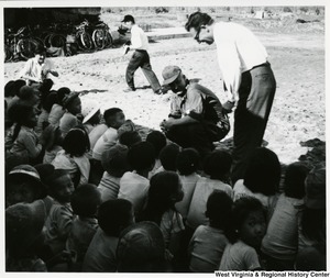 Congressman Arch A. Moore, Jr. crouched down in front of a group of children. Royall E. Norton, U.S. Regional Adviser, Region III, is standing beside Moore.