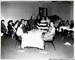 Congressman Arch A. Moore, Jr. (left) holding an American Flag with three unidentified people. There are people seated at tables around them.