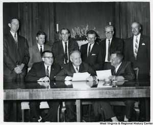 Congressman Arch A. Moore, Jr. (seated, center) meeting with eight unidentified men. They appear to be going over a document.
