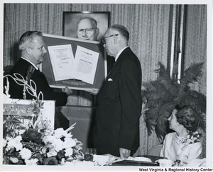 Congressman Arch A. Moore, Jr. speaking to an unidentified man while holding a framed bill for H.J.Res. 1001, a joint resolution to provide for the designation of the month of May of each year as Steelmark Month.