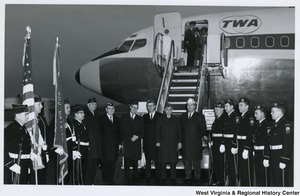 American Legion National Commander John E. Davis (center, second from right) waiting with five other men to board a plane. An honor guard is on either side of them.