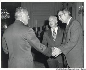 Two unidentified men are shaking hands while Governor Arch Moore (center) talks to them.
