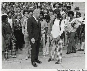 Governor Arch Moore speaking with a student from Roosevelt Jr. High School. Behind them on the steps of the capitol building is the rest of the students.