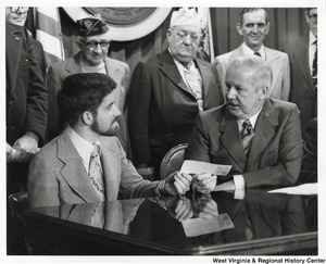 Governor Arch Moore and an unidentified man holding a check for Vietnam veterans. Behind them stand five men, two of which are veterans.