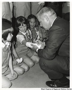 Governor Arch Moore signing the arm cast of a unidentified Brownie. Two other Brownies are watching the cast be signed.