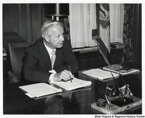 Governor Arch Moore sitting at his desk. He is speaking to someone out of frame.
