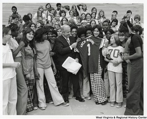 Governor Arch Moore (center) holding a sports jersey that says Arch Moore #1 on it with students at Roosevelt Jr. High School students. They are standing on the steps of the West Virigina Capitol Building.