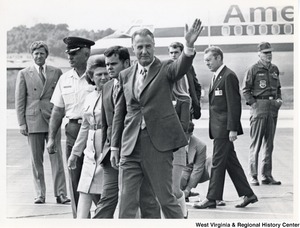 An unidentified man waving after leaving an airplane. Walking with him is Mrs. Shelley Moore (third from left) and seven unidentified people.