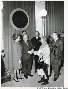Governor Arch Moore shaking the hand of unidentified woman in the capitol rotunda for his inauguration. His wife, Shelley, is standing to the left of him. Five other unidentified men are standing with them.
