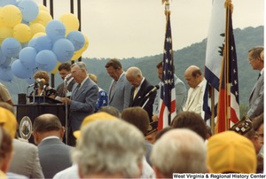 An unidentified man is leading a prayer during the Moundsville Bridge Dedication. Governor Arch Moore is standing behind the speaker (fourth from the right).