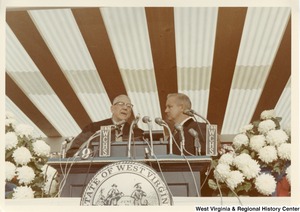 Governor Arch Moore standing behind the podium with an unidentified man.
