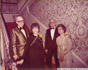 Two men and two women stand on a staircase during a reception.