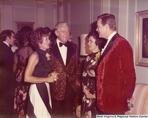 Two men and two women having a conversation at a reception. Other guests can be seen mingling behind them.