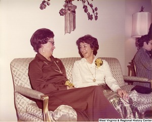 Two unidentified women sitting on a couch talking during a reception.