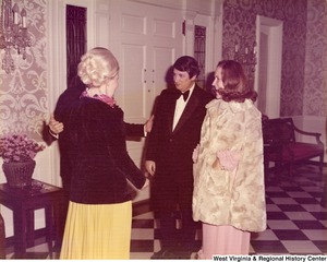 Two women and one man having a conversation at a reception. The fourth person is being hidden in the photograph by one of the women.