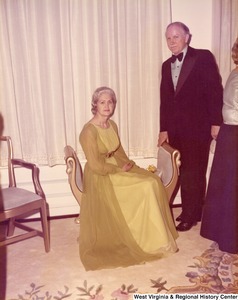 An unidentified man and woman at a reception. The woman is seated on a chair.