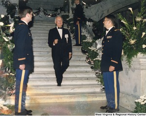 Governor Arch Moore in a tuxedo walking down the stairs. Three unidentified Army soldiers are standing at attention on the stairwell.