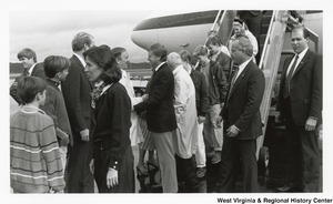 Governor Arch Moore (third from the right, white knee length coat) is being greeted after disembarking from a plane. He arrived with a group of people who are still making their way off the plane.